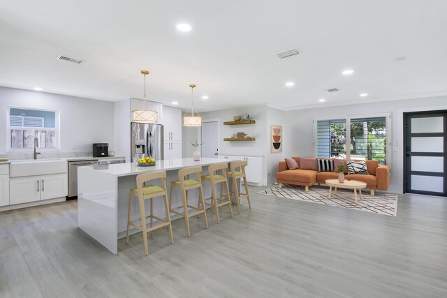 kitchen with pendant lighting, crown molding, stainless steel refrigerator with ice dispenser, light stone countertops, and white cabinetry