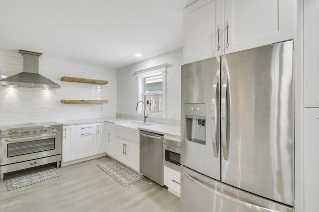 kitchen featuring sink, wall chimney exhaust hood, backsplash, white cabinets, and appliances with stainless steel finishes