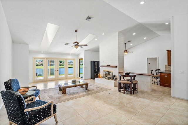 living room with a large fireplace, a skylight, light tile patterned floors, ceiling fan, and french doors