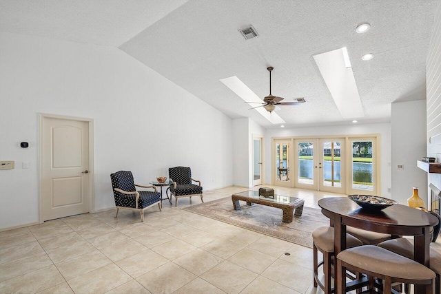 tiled living room featuring a textured ceiling, ceiling fan, french doors, and vaulted ceiling with skylight