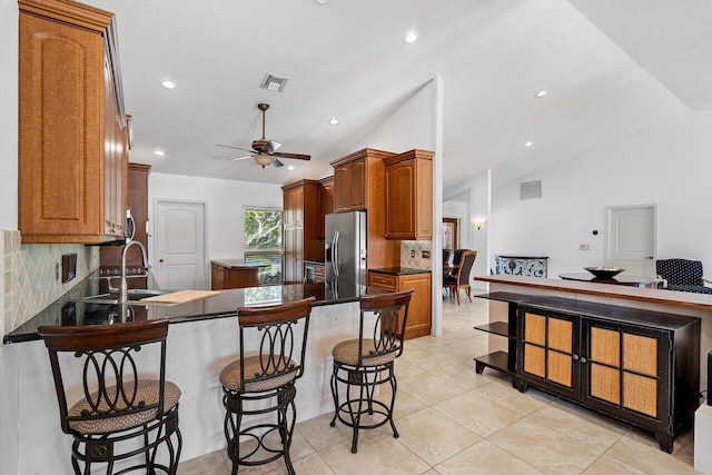 kitchen featuring stainless steel refrigerator with ice dispenser, lofted ceiling, backsplash, a kitchen breakfast bar, and sink