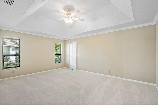 empty room featuring ceiling fan, light carpet, ornamental molding, and a raised ceiling