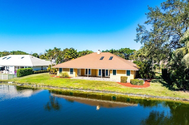 rear view of property featuring a patio area, a lawn, and a water view