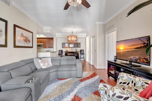 living room with ceiling fan with notable chandelier, dark hardwood / wood-style floors, ornamental molding, and sink