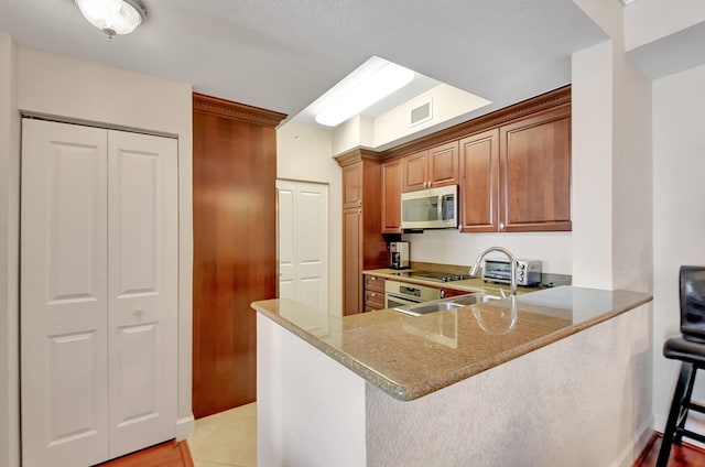 kitchen with sink, light stone counters, kitchen peninsula, a breakfast bar area, and black electric stovetop