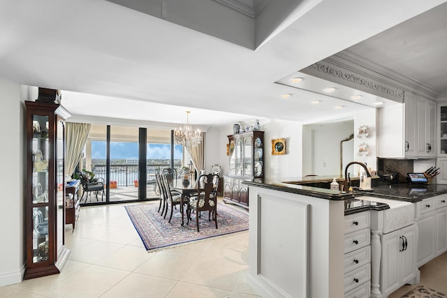 kitchen with white cabinets, backsplash, kitchen peninsula, a chandelier, and light tile patterned flooring