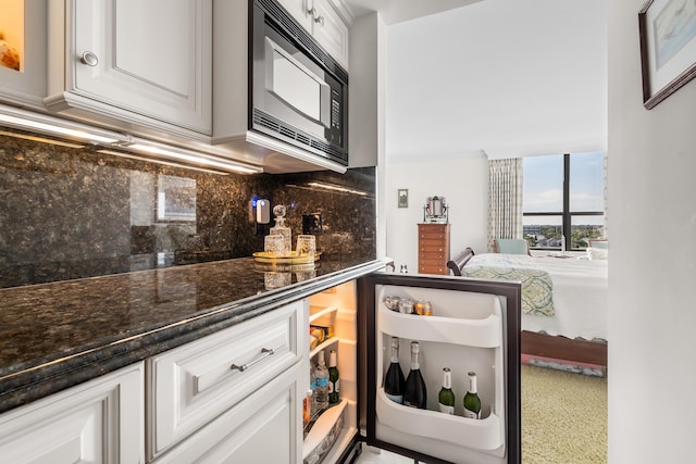 kitchen with white cabinetry, backsplash, black microwave, and dark stone countertops