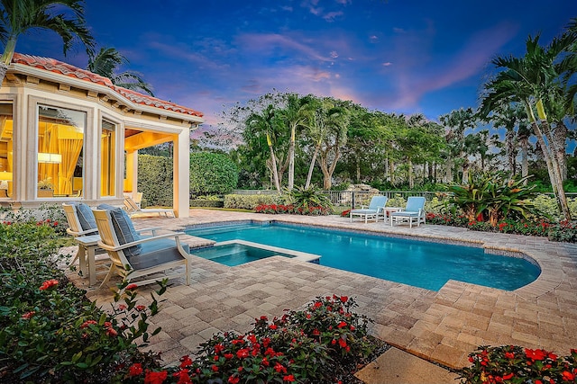 pool at dusk featuring an in ground hot tub and a patio area