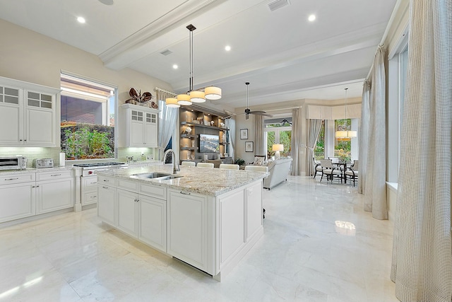 kitchen featuring sink, white cabinetry, an island with sink, decorative light fixtures, and beamed ceiling