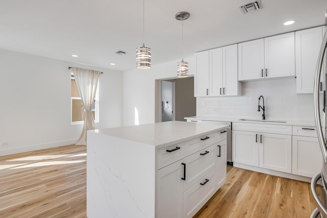 kitchen with white cabinetry, sink, a center island, hanging light fixtures, and light hardwood / wood-style flooring