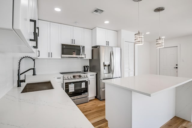 kitchen with appliances with stainless steel finishes, sink, pendant lighting, light hardwood / wood-style floors, and white cabinetry