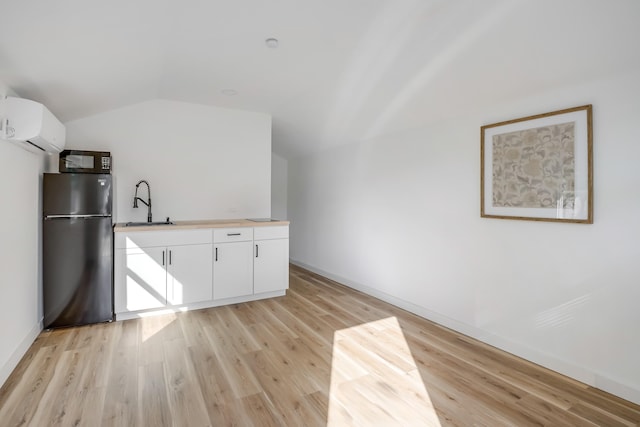 kitchen featuring a wall mounted air conditioner, stainless steel fridge, vaulted ceiling, light hardwood / wood-style flooring, and white cabinetry