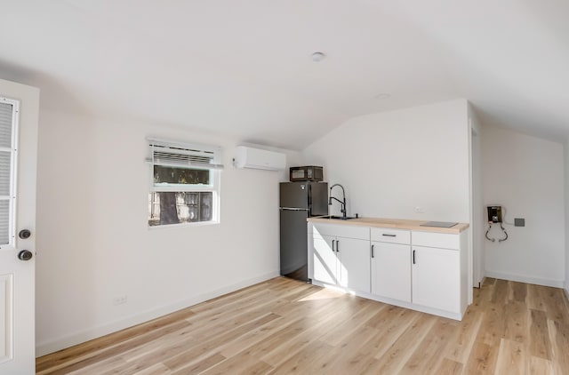 kitchen with black refrigerator, sink, white cabinets, light hardwood / wood-style floors, and lofted ceiling