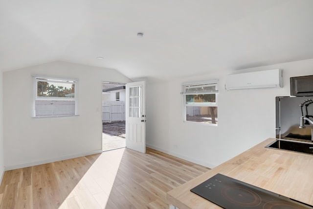 exercise room featuring light wood-type flooring, a wall mounted AC, and lofted ceiling