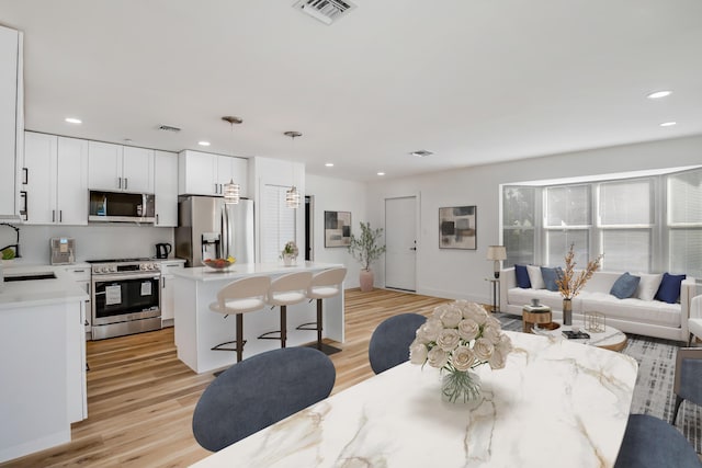 kitchen featuring light wood-type flooring, stainless steel appliances, sink, pendant lighting, and white cabinets