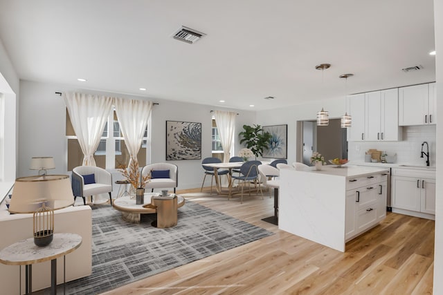 kitchen featuring decorative backsplash, sink, pendant lighting, white cabinets, and light hardwood / wood-style floors