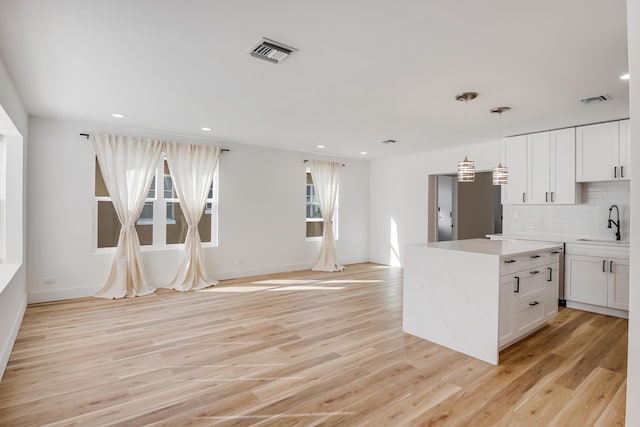 kitchen with pendant lighting, sink, light wood-type flooring, tasteful backsplash, and white cabinetry