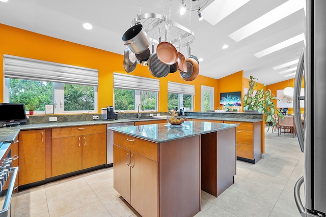 kitchen featuring vaulted ceiling with skylight, appliances with stainless steel finishes, a center island, sink, and stone counters