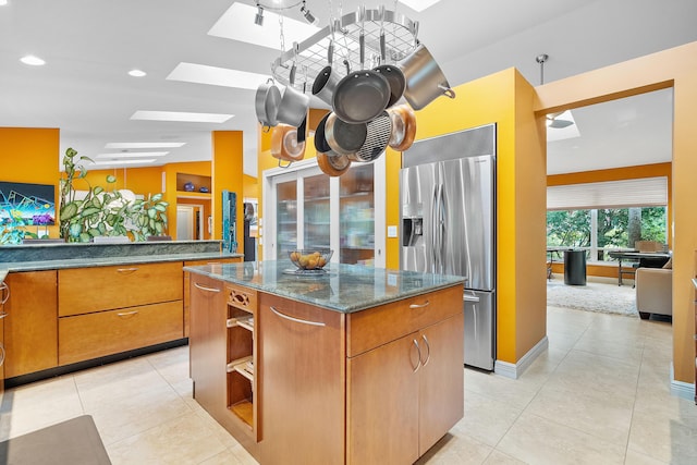 kitchen featuring vaulted ceiling with skylight, dark stone countertops, a kitchen island, stainless steel fridge with ice dispenser, and light tile patterned floors