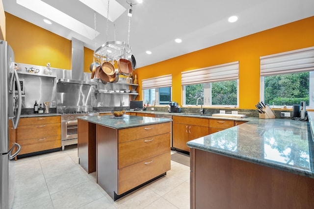 kitchen with extractor fan, kitchen peninsula, light tile patterned flooring, appliances with stainless steel finishes, and dark stone counters