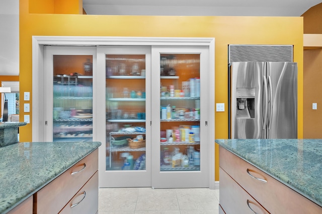 kitchen featuring stainless steel refrigerator with ice dispenser, light tile patterned floors, and stone counters