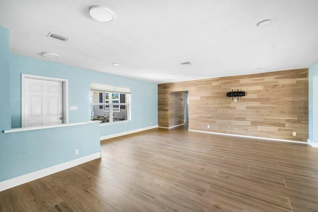 unfurnished living room with a textured ceiling, hardwood / wood-style flooring, and wooden walls