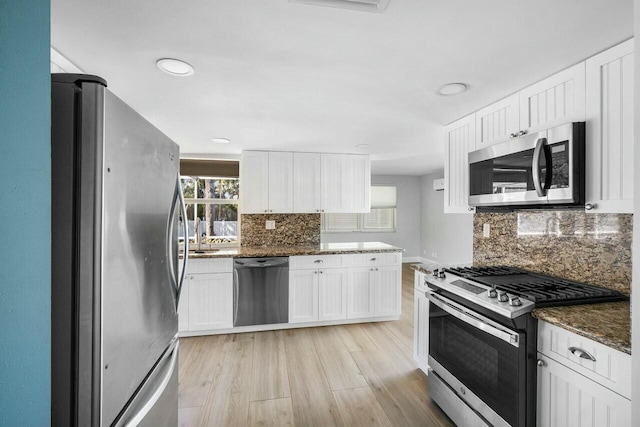 kitchen with backsplash, dark stone counters, appliances with stainless steel finishes, light hardwood / wood-style floors, and white cabinetry