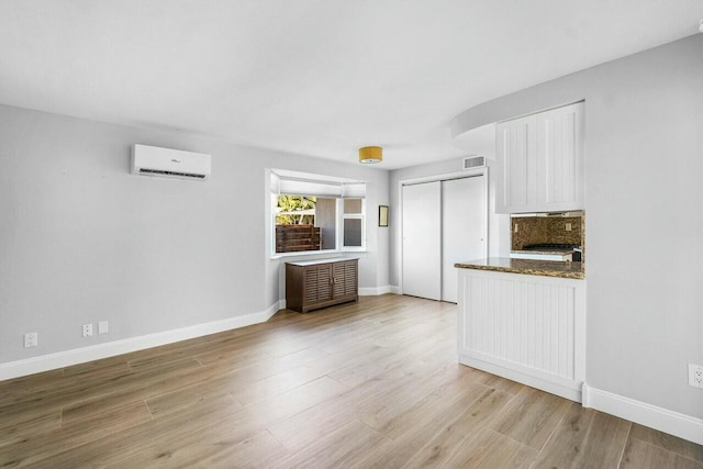 kitchen with an AC wall unit, dark stone countertops, light hardwood / wood-style floors, decorative backsplash, and white cabinets