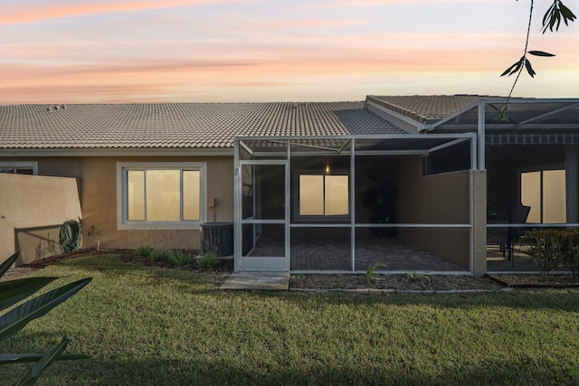 back house at dusk featuring a patio area, a lanai, and a yard