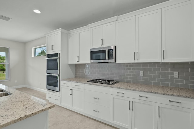 kitchen featuring light stone countertops, light tile patterned floors, tasteful backsplash, white cabinetry, and stainless steel appliances