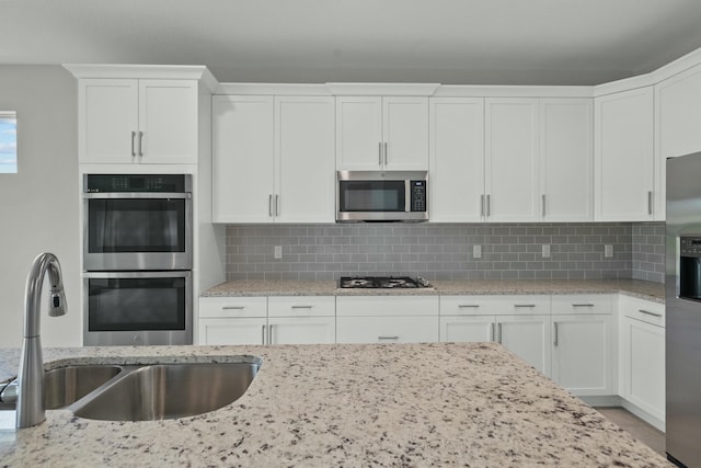 kitchen featuring backsplash, light stone counters, stainless steel appliances, sink, and white cabinets