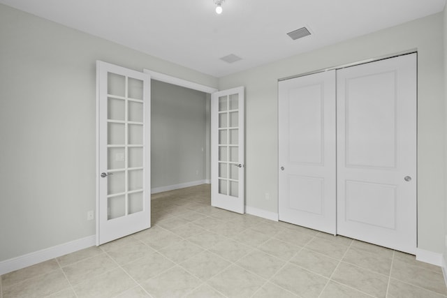 unfurnished bedroom with french doors, light tile patterned floors, and a closet