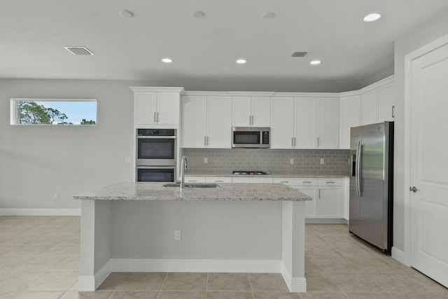 kitchen featuring decorative backsplash, appliances with stainless steel finishes, light stone counters, white cabinets, and an island with sink