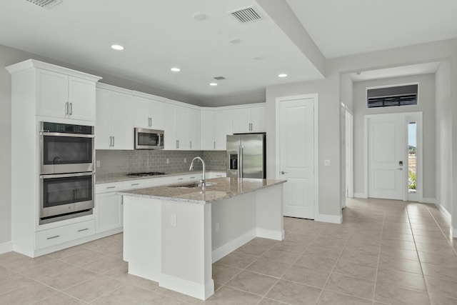 kitchen with white cabinets, light stone counters, stainless steel appliances, and an island with sink