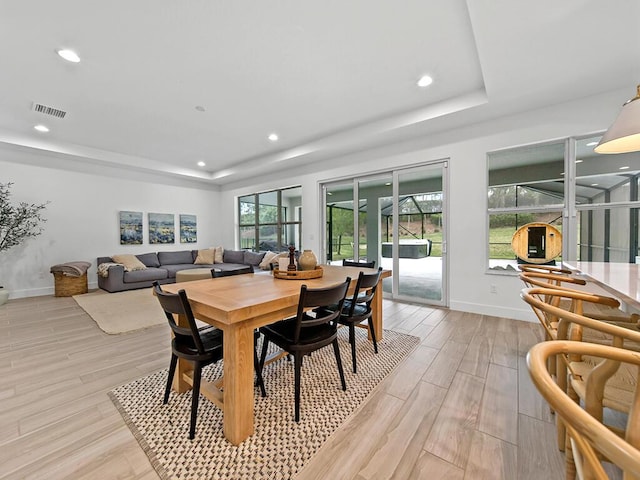 dining area featuring a raised ceiling, plenty of natural light, and light wood-type flooring