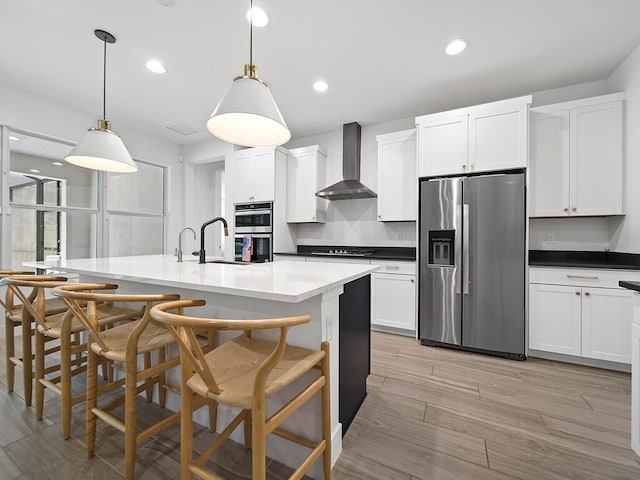 kitchen featuring sink, hanging light fixtures, wall chimney range hood, an island with sink, and appliances with stainless steel finishes