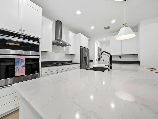 kitchen with wall chimney exhaust hood, dark stone counters, decorative light fixtures, and appliances with stainless steel finishes