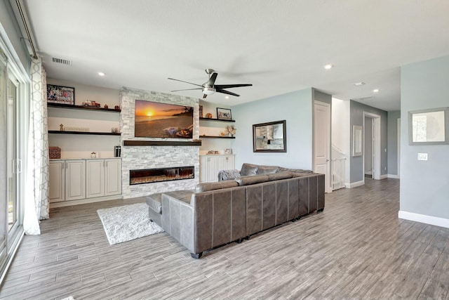 living room featuring ceiling fan, a stone fireplace, and light hardwood / wood-style flooring