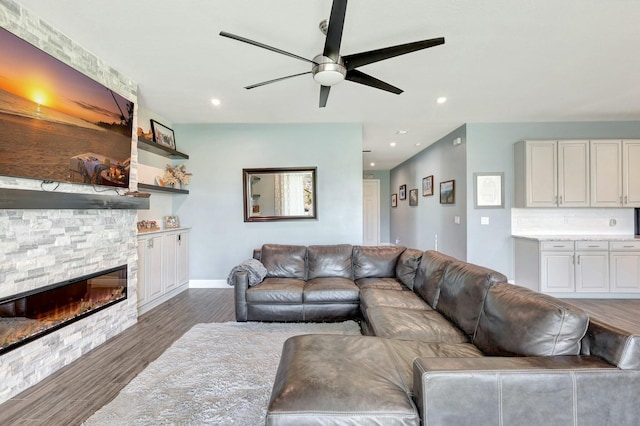 living room featuring ceiling fan, a stone fireplace, and dark wood-type flooring