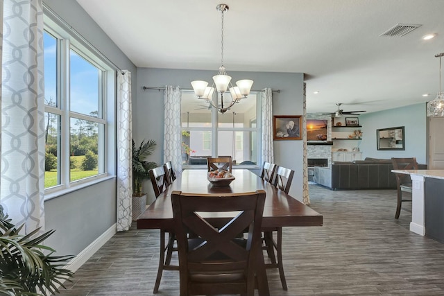 dining area with ceiling fan with notable chandelier, a stone fireplace, and dark hardwood / wood-style flooring