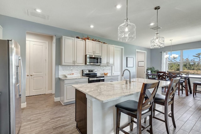 kitchen with light stone countertops, appliances with stainless steel finishes, a kitchen island with sink, sink, and pendant lighting