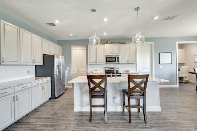 kitchen featuring light stone countertops, appliances with stainless steel finishes, a center island with sink, and pendant lighting