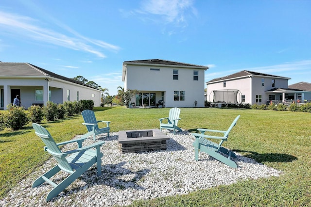 rear view of property with a lawn, a trampoline, and an outdoor fire pit