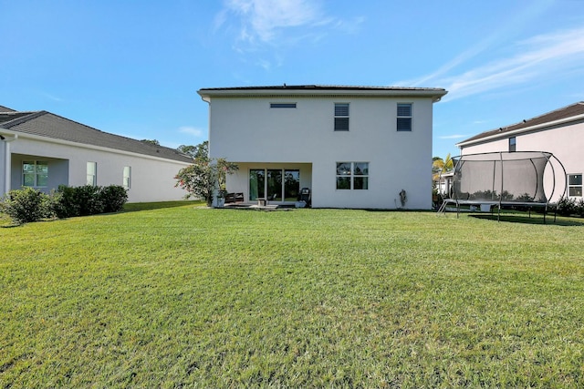 rear view of property featuring a lawn and a trampoline