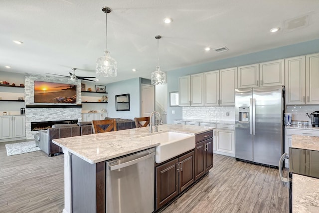 kitchen featuring appliances with stainless steel finishes, dark brown cabinetry, ceiling fan, sink, and a fireplace