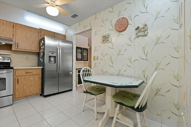 kitchen with ceiling fan, light tile patterned floors, a textured ceiling, stainless steel appliances, and extractor fan