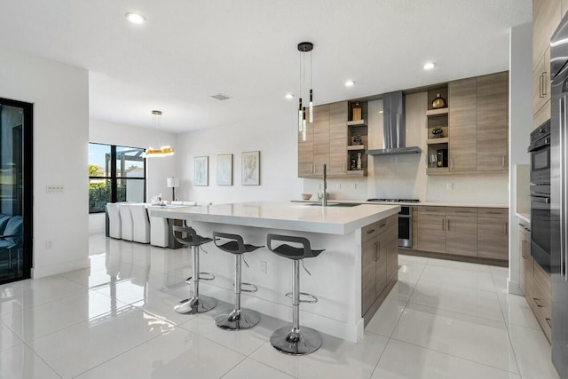 kitchen with sink, wall chimney exhaust hood, pendant lighting, a kitchen island with sink, and a breakfast bar