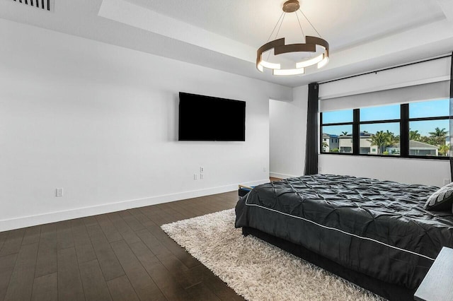 bedroom with a raised ceiling, dark wood-type flooring, and an inviting chandelier