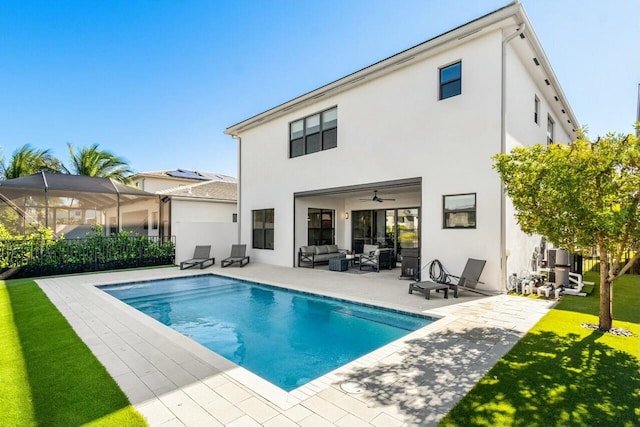 back of house featuring ceiling fan, glass enclosure, a patio area, a fenced in pool, and a lawn