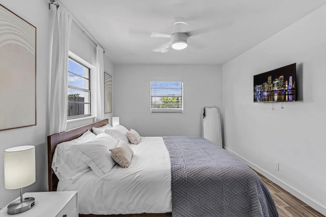 bedroom featuring ceiling fan, multiple windows, baseboards, and wood finished floors